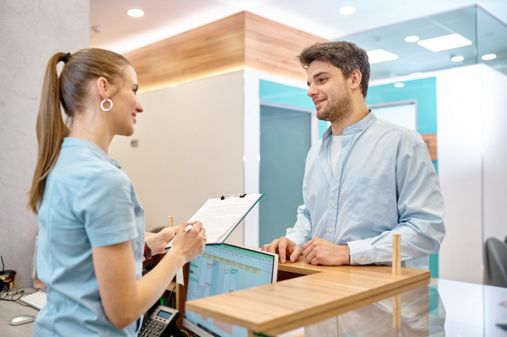 Medical office staff assisting a patient with check-in and coverage details at the front desk